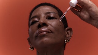 Portrait of woman with serum dropper on face against orange background