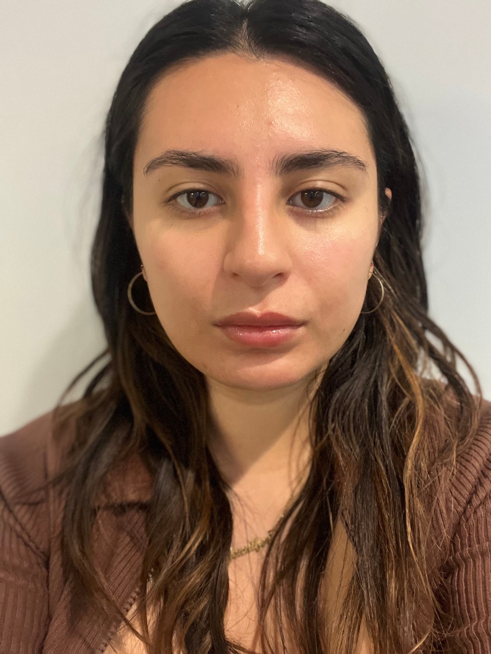 A selfie of Allure commerce writer Jennifer Hussein with no makeup on standing in front of a white background