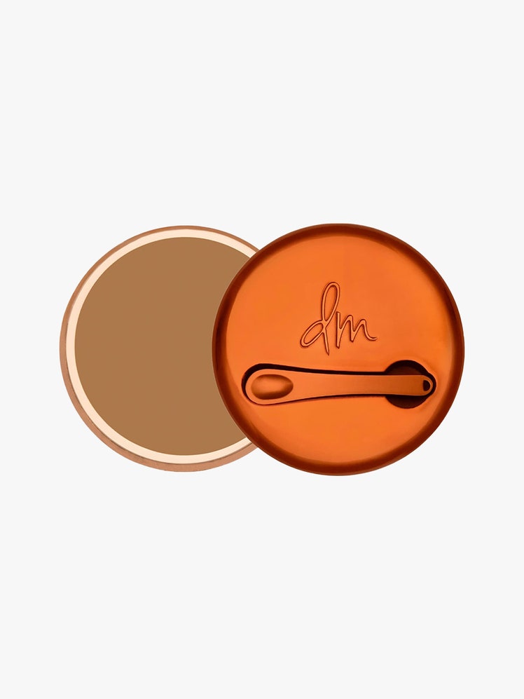 Danessa Myricks Beauty Yummy Skin Blurring Balm Powder top view of a jar of foundation balm with orange chrome lid ajar on light gray background