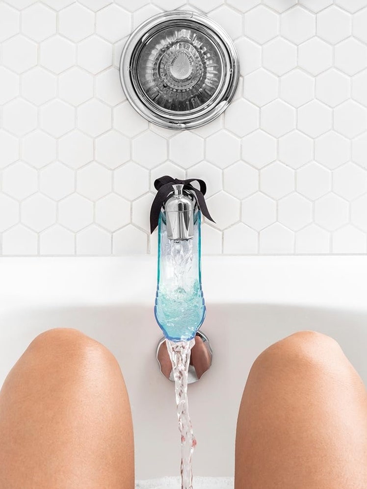 Lovability WaterSlyde Aquatic Stimulator transparent turquoise water slide stimulator attached to a bathtub water spigot in a white tub with a person's legs in front of it